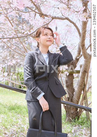 A young woman in a business suit poses under cherry blossoms – an image of spring job hunting. 139402507
