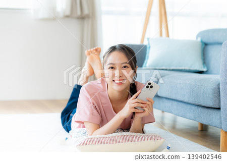 在房間裡操作智慧型手機的年輕女子 在房間裡操作智慧型手機的年輕女子 139402546
