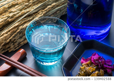 一幅日式風格的圖片，畫面中有清酒、稻穗、醃菜和筷子。 139402588