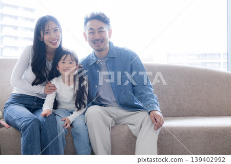 A family's lifestyle image of buying a home, smiling and looking at the camera by the window of their new apartment. 139402992