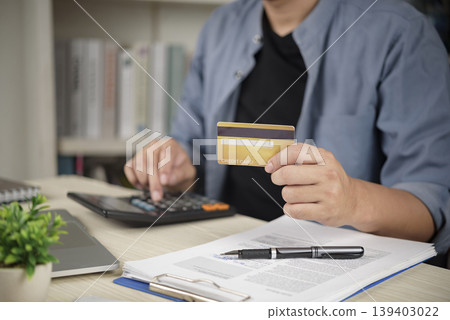 Man holding credit card and using calculator for financial planning, paying bills, checking debt balance, and online shopping at home office desk. Man holding credit card and using calculator for financial planning, paying bills, checking debt balance, and online shopping at home office desk. 139403022