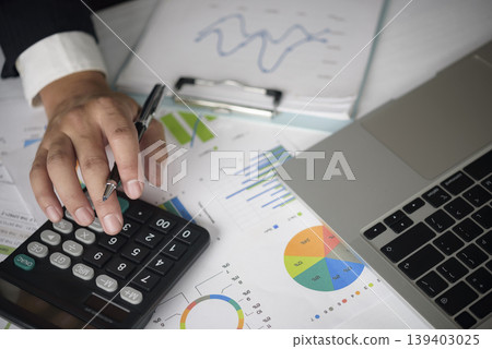 Close up businessman hand using calculator and writing on financial report with charts and laptop on desk. Professional accountant analyzing budget and business plan in office. Finance concept. Close up businessman hand using calculator and writing on financial report with charts and laptop on desk. Professional accountant analyzing budget and business plan in office. Finance concept. 139403025