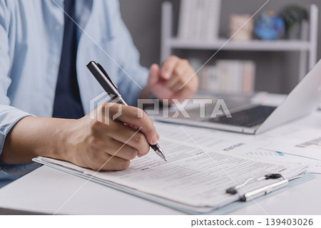 Businessman hand filling out tax return form or insurance application document. Financial paperwork, audit compliance and business contract signing concept on office desk. Businessman hand filling out tax return form or insurance application document. Financial paperwork, audit compliance and business contract signing concept on office desk. 139403026