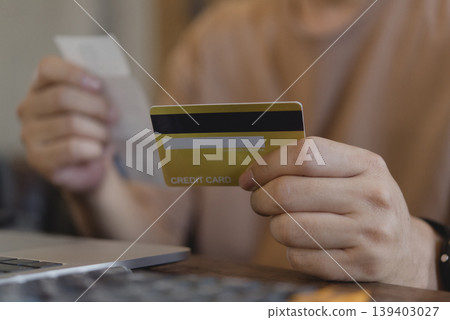 Man holding gold credit card and checking shopping receipt near laptop. Online payment, e-commerce and household expense budget calculation concept. Man holding gold credit card and checking shopping receipt near laptop. Online payment, e-commerce and household expense budget calculation concept. 139403027