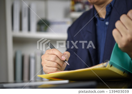 Professional man in a suit checking and filling out paperwork, reviewing a report, or taking notes in a file folder. 139403039