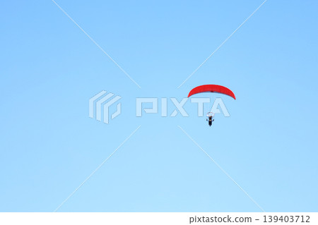 Red parachute soars against vast, clear blue sky Red parachute soars against vast, clear blue sky 139403712