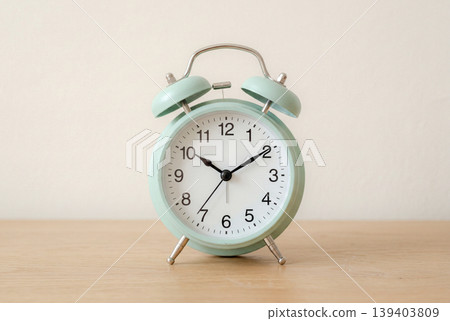 A light green alarm clock placed on a wooden surface. 139403809