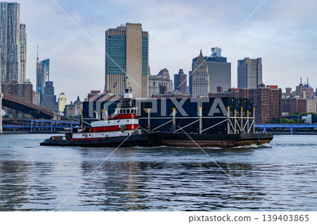 Tugboat pushing barge at Brooklyn bridge. Barge and tugboat in Hudson river, New York. Manhattan cityscape. Amazing scenery over skyscraper in New York. Way to Manhattan Tugboat pushing barge at Brooklyn bridge. Barge and tugboat in Hudson river, New York. Manhattan cityscape. Amazing scenery over skyscraper in New York. Way to Manhattan 139403865