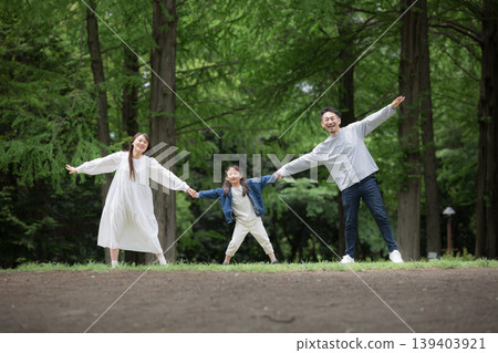 A happy family lifestyle: holding hands in a park surrounded by fresh greenery, smiling and looking at the camera. (Full body shot) A happy family lifestyle: holding hands in a park surrounded by fresh greenery, smiling and looking at the camera. (Full body shot) 139403921