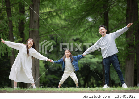 A happy family lifestyle: holding hands in a park surrounded by fresh greenery, smiling and looking at the camera. (Full body shot) A happy family lifestyle: holding hands in a park surrounded by fresh greenery, smiling and looking at the camera. (Full body shot) 139403922
