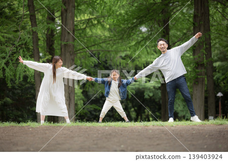 A happy family lifestyle: holding hands in a park surrounded by fresh greenery, smiling and looking at the camera. (Full body shot) A happy family lifestyle: holding hands in a park surrounded by fresh greenery, smiling and looking at the camera. (Full body shot) 139403924