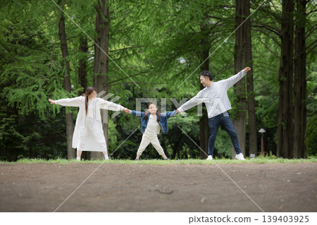 A happy family lifestyle: holding hands in a park surrounded by fresh greenery, smiling and looking at the camera. (Full body shot) A happy family lifestyle: holding hands in a park surrounded by fresh greenery, smiling and looking at the camera. (Full body shot) 139403925