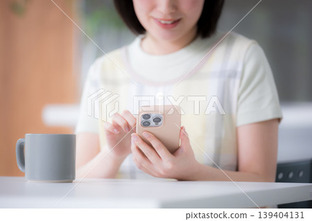 A woman wearing an apron like a housewife, holding a smartphone, taps, searches, finds, posts reviews, etc., for kitchen and dining. 139404131