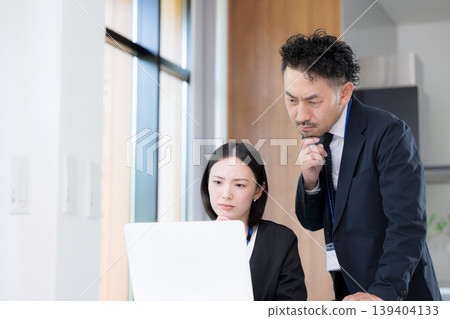 A team of businessmen, a boss and his male subordinate, are working on desk jobs, their expressions serious and thoughtful, as they ponder and struggle with their tasks in front of their computers. A team of businessmen, a boss and his male subordinate, are working on desk jobs, their expressions serious and thoughtful, as they ponder and struggle with their tasks in front of their computers. 139404133