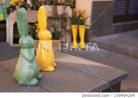 Vibrant ceramic rabbits standing on an outdoor stone ledge with blurred spring decorations 139404284