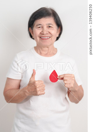 Elderly woman with red Blood drop paper for concept of June World Blood Donor day, Donation, April Hemophilia awareness day, May Thalassemia Day, Anemia awareness, June Sickle Cell and Blood Disorders 139406250