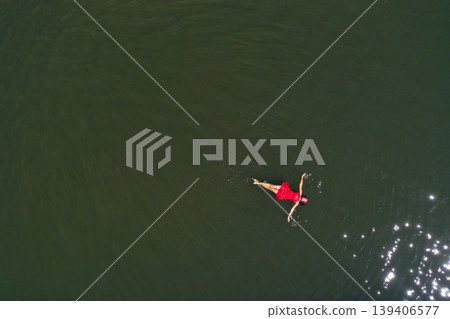 Aerial view of woman in red dress floats peacefully in a lake, embracing serenity and solitude Aerial view of woman in red dress floats peacefully in a lake, embracing serenity and solitude 139406577