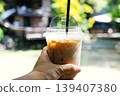 Close up woman hand holding iced latte coffee in plastic glass at cafe in bright day natural background 139407380