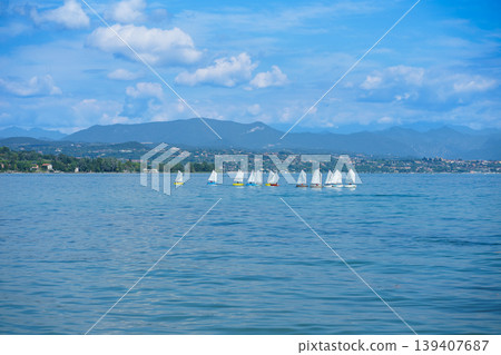 Group of small sailboats on Lake Garda with scenic mountains and blue sky, peaceful water landscape in Italy, summer sailing and travel concept Group of small sailboats on Lake Garda with scenic mountains and blue sky, peaceful water landscape in Italy, summer sailing and travel concept 139407687