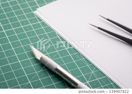Professional knife and tweezers near blank white paper on cutting mat Professional knife and tweezers near blank white paper on cutting mat 139407822