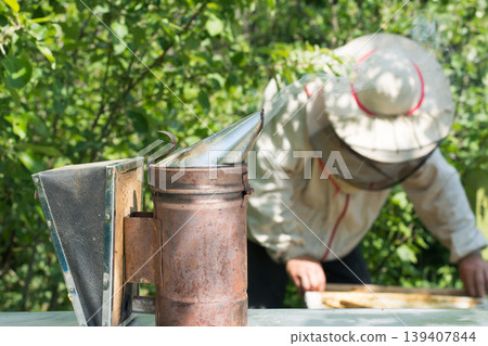 Bee smoker tool against the beekeeper with beehives Bee smoker tool against the beekeeper with beehives 139407844