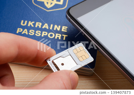 Man inserting tray for SIM card and micro SD memory card to the mobile phone near Ukrainian biometric passport. Registration and identification SIM card for mobile phone using passport Man inserting tray for SIM card and micro SD memory card to the mobile phone near Ukrainian biometric passport. Registration and identification SIM card for mobile phone using passport 139407873