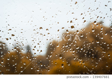 Drops of rain on window against gloomy rainy sky and golden trees on the background Drops of rain on window against gloomy rainy sky and golden trees on the background 139407881
