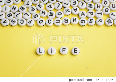 The word LIFE made of white plastic blocks on yellow background with many letters on the top 139407886