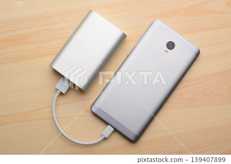 Silver smartphone charging with a power bank on a light wooden background 139407899