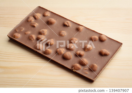 Bar of milk chocolate with nuts on light wooden background Bar of milk chocolate with nuts on light wooden background 139407907