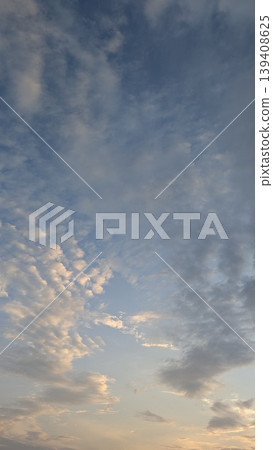 Vertical view shows blue sky, soft sunrise clouds. Golden light illuminates white, grey cloud patterns. Serene atmosphere for nature backgrounds, spiritual themes, weather concepts, peaceful designs. 139408625