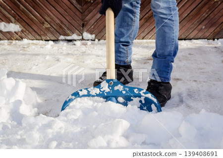 Young man shoveling snow in the driveway near the garage after a heavy snow in order to make way for a car 139408691