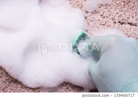 Cleaning carpet by a detergent with a lot of foam. Hand in green rubber glove washing carpet by a green sponge. Spring cleaning in house Cleaning carpet by a detergent with a lot of foam. Hand in green rubber glove washing carpet by a green sponge. Spring cleaning in house 139408717