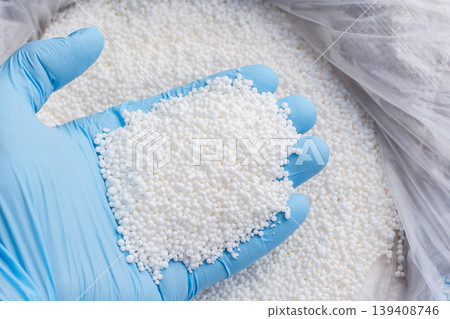 Closeup photo of a hand in blue glove holds white fertilizer for plants. Big bag with chemical NPK fertilizer for plants 139408746