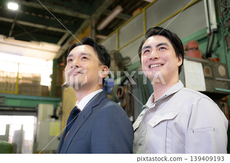 在一家工廠裡,一位商人和一位工人面帶微笑,抬頭望向未來,展現了兩人之間的相互信任關係。 在一家工廠裡,一位商人和一位工人面帶微笑,抬頭望向未來,展現了兩人之間的相互信任關係。 139409193
