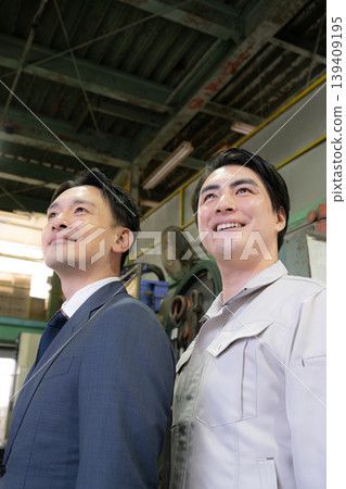 在一家工廠裡,一位商人和一位工人微笑著望著未來,展現了兩人之間互信的關係。 (豎圖) 在一家工廠裡,一位商人和一位工人微笑著望著未來,展現了兩人之間互信的關係。 (豎圖) 139409195