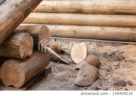 Stacked round logs and freshly cut timber beside a partially built log cabin 139409216