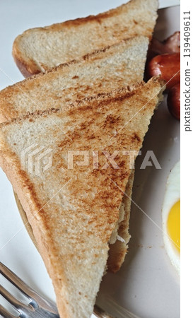 Toasted whole grain bread slices arranged on a plate with a fried egg and sausage, showcasing a simple breakfast setting with cutlery nearby Toasted whole grain bread slices arranged on a plate with a fried egg and sausage, showcasing a simple breakfast setting with cutlery nearby 139409611