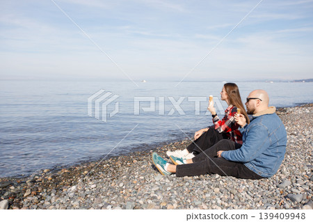 Lifestyle portrait of couple sitting on beach and eating ice cream Lifestyle portrait of couple sitting on beach and eating ice cream 139409948
