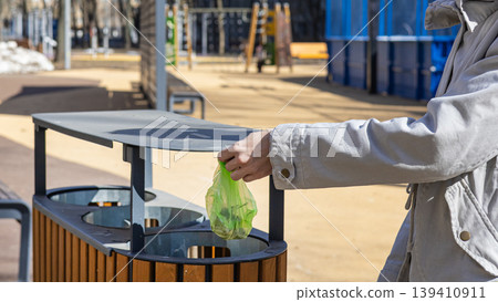 Woman using public dog waste station with poo bag dispenser outdoors. Woman using public dog waste station with poo bag dispenser outdoors. 139410911