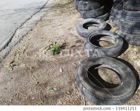 : Stack of discarded black car tires piled along a dirt roadside. The image captures environmental waste and industrial materials left outdoors, highlighting themes of recycling and pollution : Stack of discarded black car tires piled along a dirt roadside. The image captures environmental waste and industrial materials left outdoors, highlighting themes of recycling and pollution 139411251