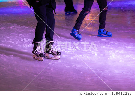 Several people in various ice skates glide smoothly on a vibrant, illuminated purple rink, embodying the joy of winter recreation and holiday leisure Several people in various ice skates glide smoothly on a vibrant, illuminated purple rink, embodying the joy of winter recreation and holiday leisure 139412283