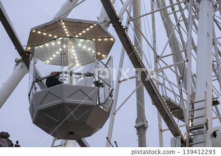 An individual experiences a serene, illuminated night ride within a modern Ferris wheel gondola, offering a tranquil urban leisure and panoramic observation adventure An individual experiences a serene, illuminated night ride within a modern Ferris wheel gondola, offering a tranquil urban leisure and panoramic observation adventure 139412293