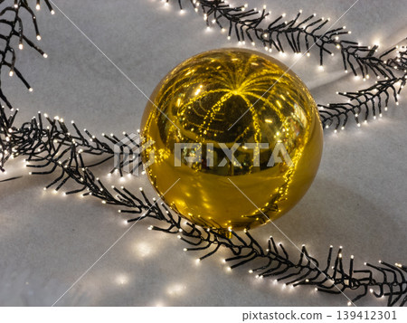 Bright golden christmas ornament sphere reflecting numerous twinkling lights from a decorative holiday garland, evoking festive warmth and celebration mood Bright golden christmas ornament sphere reflecting numerous twinkling lights from a decorative holiday garland, evoking festive warmth and celebration mood 139412301