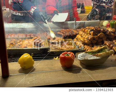 Street food vendor grilling savory sausages, succulent kebabs, and hot dogs, offering a rich culinary experience at an outdoor market 139412303