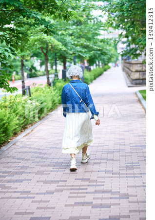 A senior woman walking down a tree-lined street, seen from behind and in full. A senior woman walking down a tree-lined street, seen from behind and in full. 139412315
