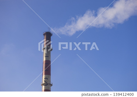Tall industrial chimney emitting thick white smoke against a clear blue sky, symbolizing industrial activity, energy production, and environmental pollution Tall industrial chimney emitting thick white smoke against a clear blue sky, symbolizing industrial activity, energy production, and environmental pollution 139412400