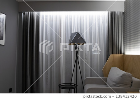 Contemporary interior design showcases a modern geometric floor lamp and sheer curtains, creating a tranquil and stylish atmosphere for home comfort and relaxation Contemporary interior design showcases a modern geometric floor lamp and sheer curtains, creating a tranquil and stylish atmosphere for home comfort and relaxation 139412420