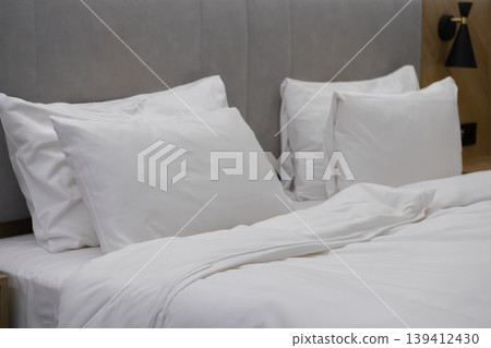 A comfortable hotel bed neatly made with crisp white linen and soft pillows, emphasizing inviting luxury for modern hospitality and home decor A comfortable hotel bed neatly made with crisp white linen and soft pillows, emphasizing inviting luxury for modern hospitality and home decor 139412430