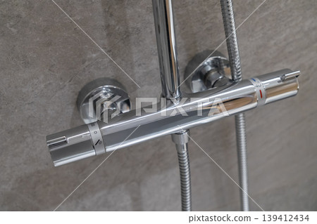 Modern chrome thermostatic shower mixer tap mounted on a grey tiled wall, featuring temperature controls and 40 marking for precise water regulation in a contemporary bathroom Modern chrome thermostatic shower mixer tap mounted on a grey tiled wall, featuring temperature controls and 40 marking for precise water regulation in a contemporary bathroom 139412434